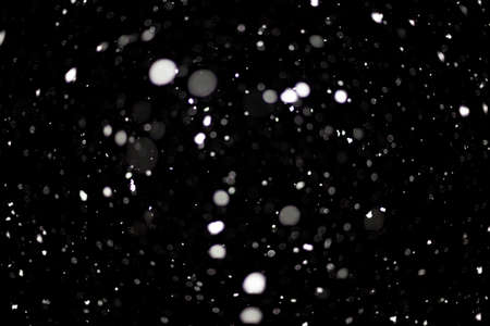 Snowstorm texture. Bokeh lights on black background, shot of flying snowflakes in the airの写真素材