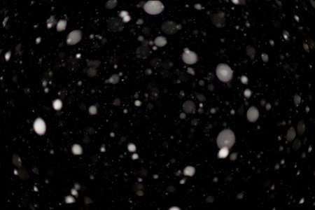 Snowstorm texture. Bokeh lights on black background, shot of flying snowflakes in the airの写真素材