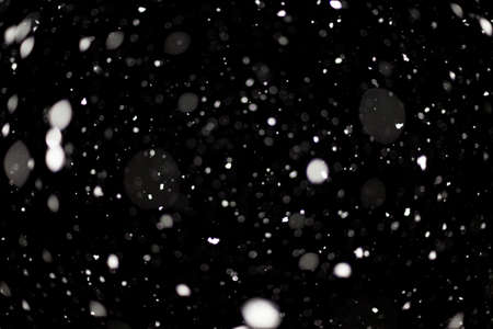 Snowstorm texture. Bokeh lights on black background, shot of flying snowflakes in the airの写真素材