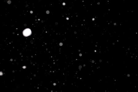 Snowstorm texture. Bokeh lights on black background, shot of flying snowflakes in the airの写真素材