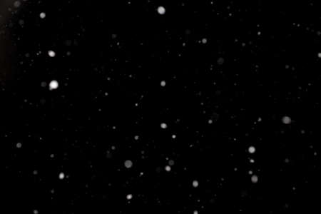 Snowstorm texture. Bokeh lights on black background, shot of flying snowflakes in the airの写真素材