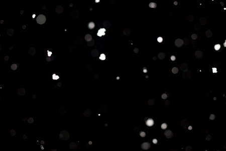 Snowstorm texture. Bokeh lights on black background, shot of flying snowflakes in the airの写真素材