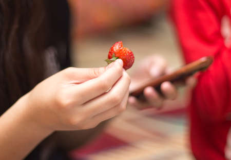 in the hand of a girl sweet fresh strawberries and a smartphoneの写真素材