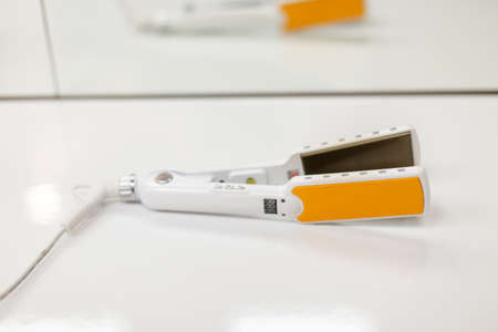 Curling tongs with ceramic plates on a white tableの写真素材