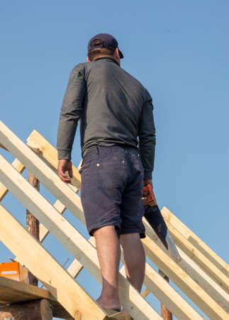 Roofer, carpenter on the roof, he closes the roof of a small and cozy houseの写真素材