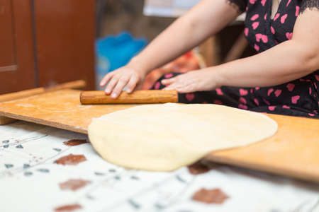 Hands working with bread dough recipe preparation. Female hands making dough. Women's hands roll out the dough. Mom rolls dough on a kitchen board with a rolling pinの写真素材