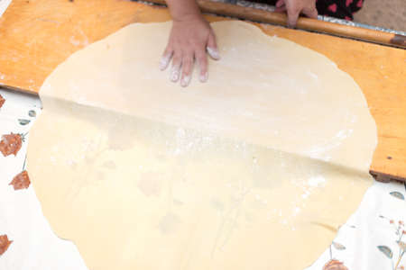Hands working with bread dough recipe preparation. Female hands making dough. Women's hands roll out the dough. Mom rolls dough on a kitchen board with a rolling pinの写真素材