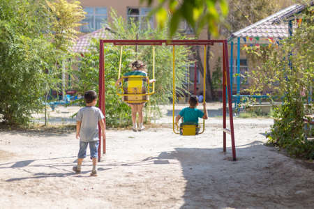 A child swinging on the playground on a sunny summer day in the park. Children's swing. Courtyard of a school or kindergarten and a playground. Little boys fly high in the air on a swing. Kid playingの写真素材