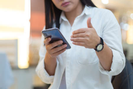Female hand holds a smartphone. She uses a smartphone and sits in the office. Sexy girlの写真素材
