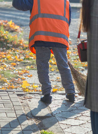 A cleaning lady cleans the dead side of the maple leaves from the sidewalk.