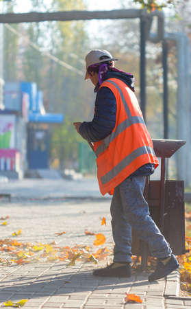 A cleaning lady cleans the dead side of the maple leaves from the sidewalk.の写真素材