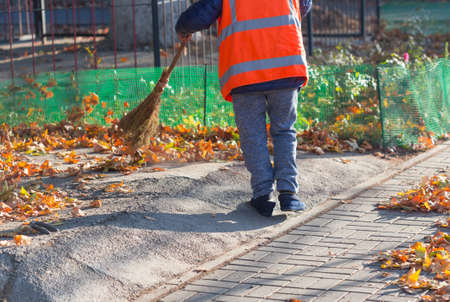 A cleaning lady cleans the dead side of the maple leaves from the sidewalk.の写真素材