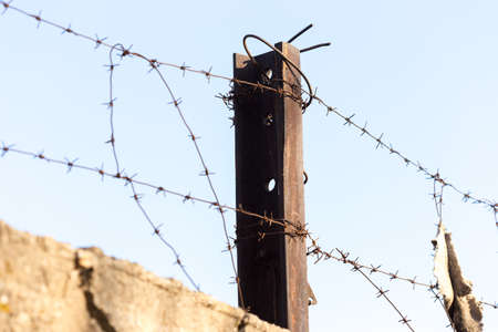 barbed wire with spikes over a concrete fence in the background of blue skyの写真素材