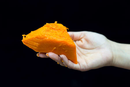 Female hand holds a piece of fresh pumpkin on a black backgroundの写真素材