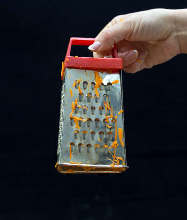 Female hand holds a piece of fresh pumpkin and rubs it on a metal kitchen grater on a black backgroundの写真素材