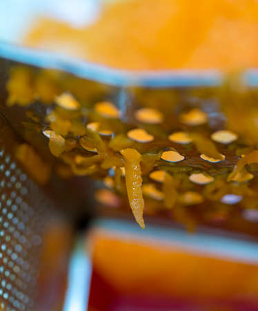 A woman's hand holds a piece of fresh pumpkin and rubs it on a metal kitchen grater.の写真素材