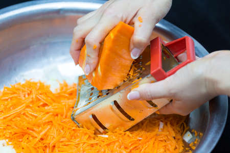 A woman's hand holds a piece of fresh pumpkin and rubs it on a metal kitchen grater.の写真素材