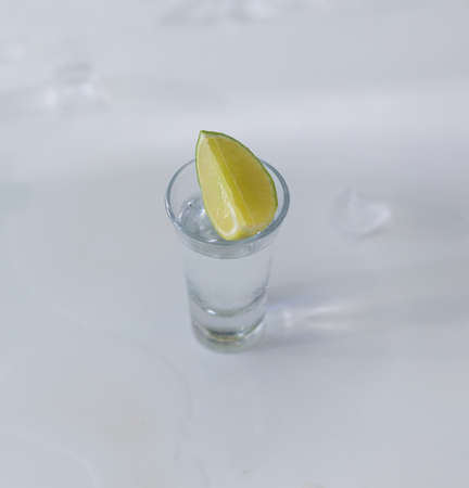 glasses of silver tequila, a slice of lime and pieces of ice on the tableの写真素材