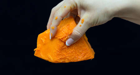 Female hand holds a piece of fresh pumpkin on a black backgroundの写真素材