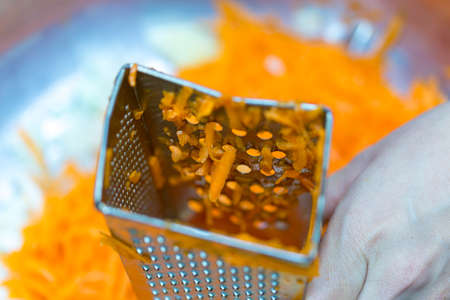A woman's hand holds a piece of fresh pumpkin and rubs it on a metal kitchen grater.の写真素材