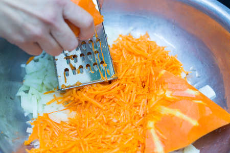A woman's hand holds a piece of fresh pumpkin and rubs it on a metal kitchen grater.の写真素材