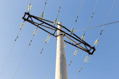 Concrete pillar power lines with steel traverses, porcelain insulators and high-voltage wires on a background of the clear blue skyの写真素材