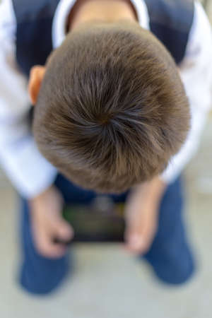 Young boy play online games on a smartphone. Beautiful teenager use phone from sideの写真素材