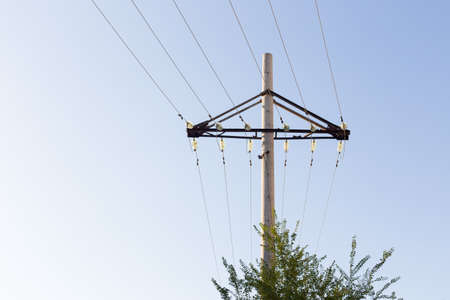 Concrete pillar power lines with steel traverses, porcelain insulators and high-voltage wires on a background of the clear blue skyの写真素材