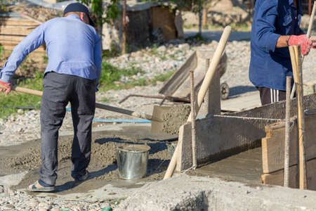 Manually mixing cement mortar with a shovel on a sheet of iron and loading into a bucketの写真素材