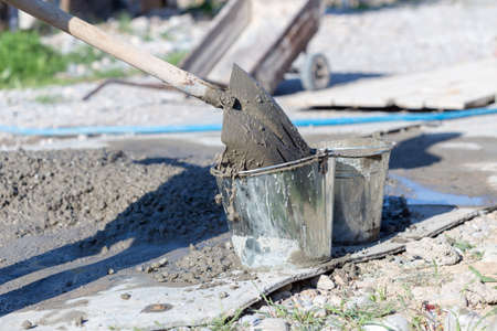 Manually mixing cement mortar with a shovel on a sheet of iron and loading into a bucketの写真素材