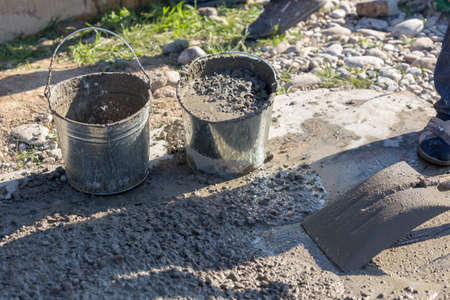 Manually mixing cement mortar with a shovel on a sheet of iron and loading into a bucketの写真素材
