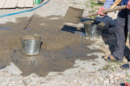 Manually mixing cement mortar with a shovel on a sheet of iron and loading into a bucketの写真素材
