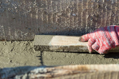 The male hand levels a cement mortar with a rake. Concrete foundation for homeの写真素材