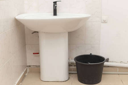 bathroom with white sink, modern black techno style faucet, next to a black plastic bucket