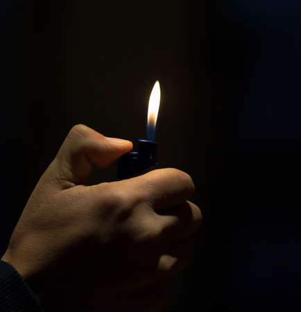 Male hand holding a lighter with a big flame and a cigaretteの写真素材