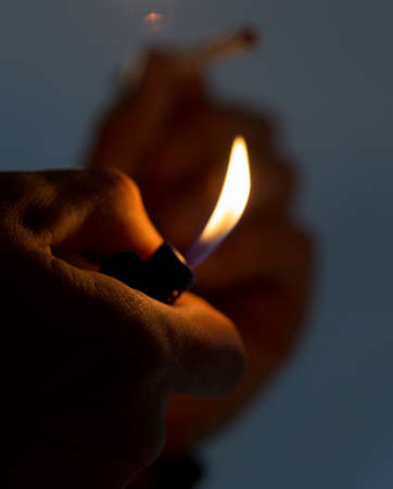 Male hand holding a lighter with a big flame and a cigaretteの写真素材