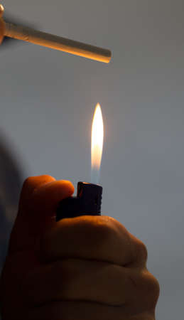 Male hand holding a lighter with a big flame and a cigaretteの写真素材