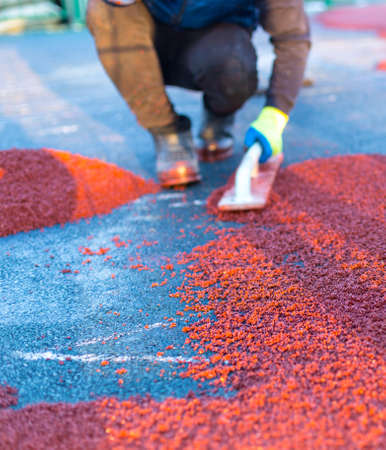 red rubber covering for the playground, the master smoothes the soft rubber crumb by hand. Soft covering for sports floors. Rubber mulch for safety and injury prevention.の写真素材