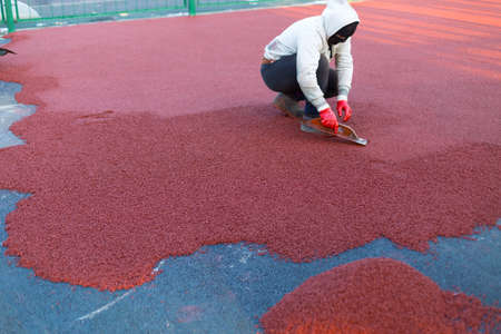 red rubber covering for the playground, the master smoothes the soft rubber crumb by hand. Soft covering for sports floors. Rubber mulch for safety and injury prevention.の写真素材