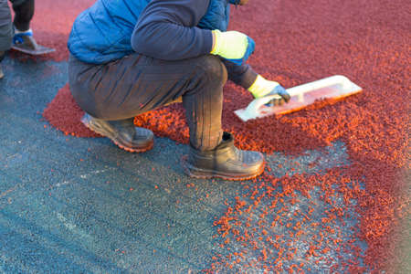 red rubber covering for the playground, the master smoothes the soft rubber crumb by hand. Soft covering for sports floors. Rubber mulch for safety and injury prevention.の写真素材