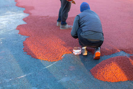 red rubber covering for the playground, the master smoothes the soft rubber crumb by hand. Soft covering for sports floors. Rubber mulch for safety and injury prevention.の写真素材