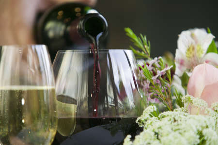 Pouring red wine into a glass sitting on a table in a fine restaurant setting 