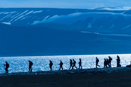 Silhouetted group of hikers along an inlet in Barentsoya, Svalbard, Norway within the arctic circle.の写真素材