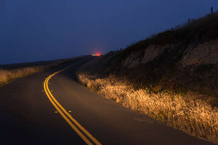 Red car tail lights on a curved road on a foggy night in Inverness, California, USAの写真素材