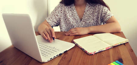 Online e learning at home background image with a hand of a girl on a laptop writing and a notebook...