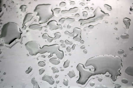 water drops with irregular shapes on a flat reflective glass surface with nice light contrastの写真素材