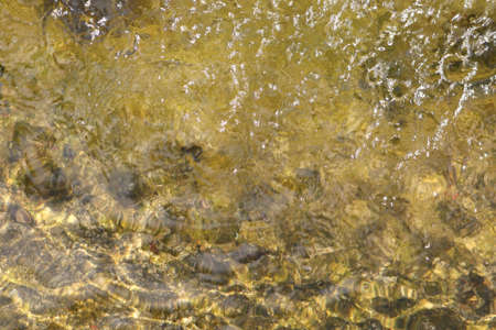 golden light reflections in the water of a fountain - contrast between rough and smooth waves background textureの写真素材