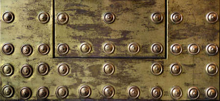 rusty and damaged metal plate with golden tone - worn steampunk background surface with screws and scratchesの写真素材