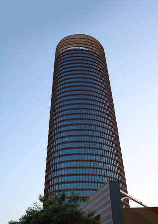 Torre Sevilla or Tower of Seville, big cylindrical building of offices, seen from below in...