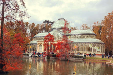 Lanscape with crystal Palace in Retiro Park of Madrid in autumn at sunset with a cloudy sky and red...